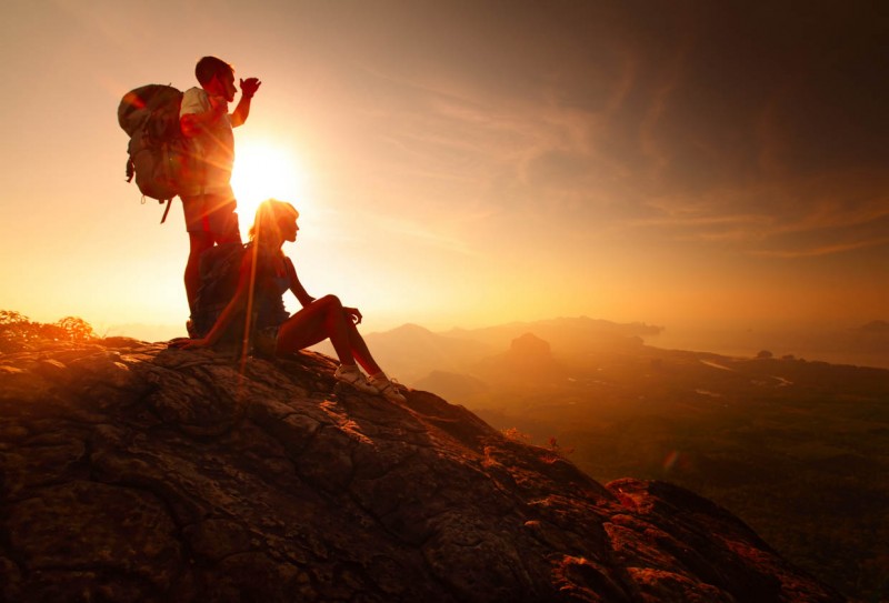 Two hikers enjoying sunrise from top of a mountain